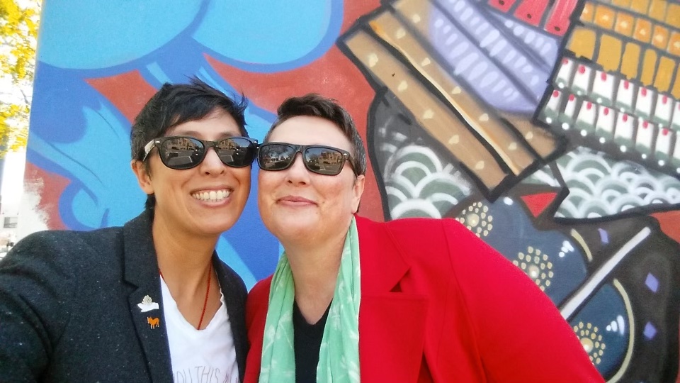 Photo of Williams, stylish Asian American of the LGBTQ+ variety in black sunglasses and Jonet, who is a white, fat, first generation, working-class LGBTQ+.