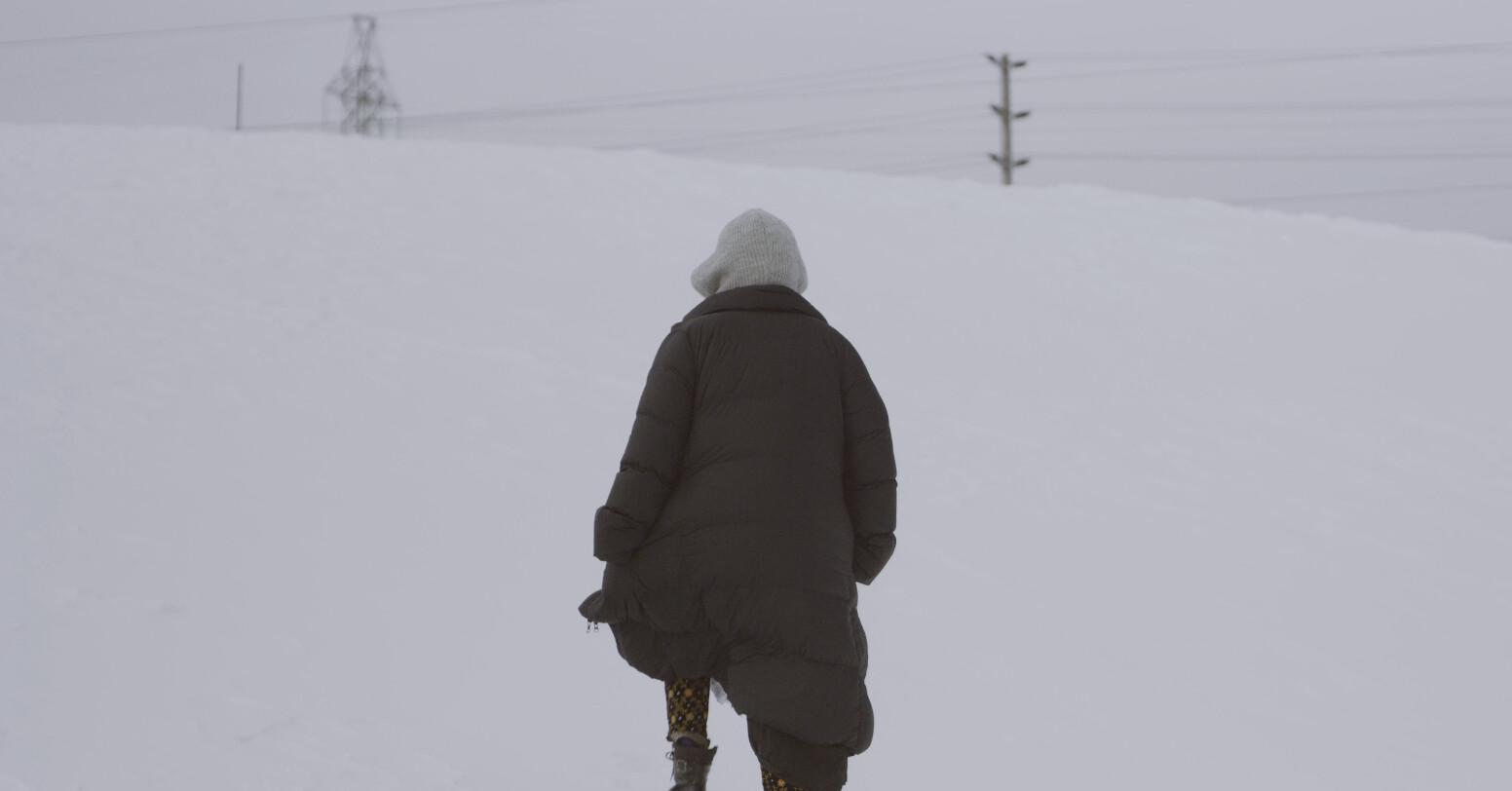 A woman facing away walks into the white snowy land